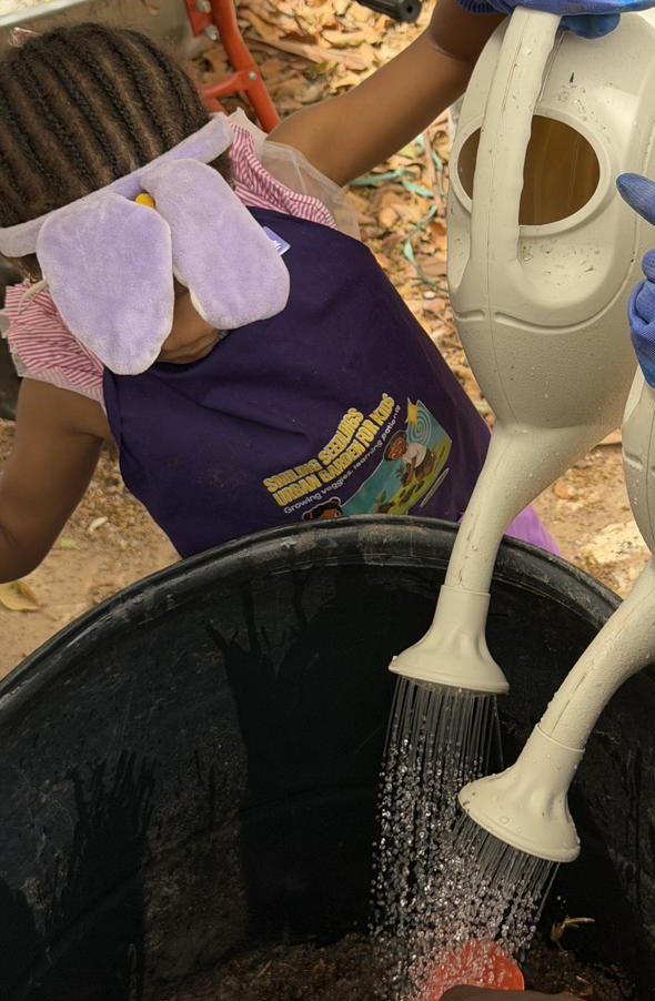 A child in a Smiling Seedlings branded apron watering with a garden can